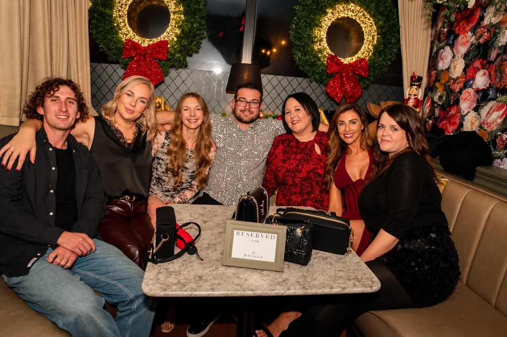 A big group round a booth table, dressed up for a Christmas night out