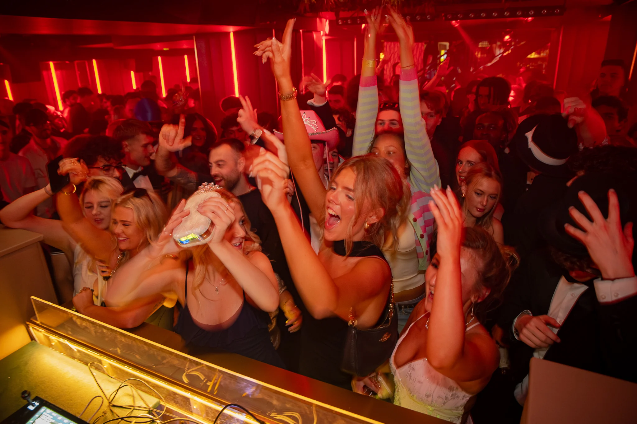 A packed dance floor with hands in the air under red light at Baluga